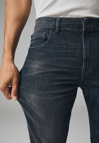 A sötét farmernadrág slim fit szabással, finom kopással és klasszikus ötpocket kialakítással rendelkezik. A derékpánton gomb és cipzár található.