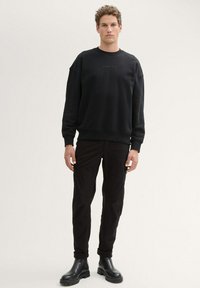 Svart, texturerad sweatshirt med rund halsringning, med subtil branding. Kombination med svarta cargobyxor och ankelboots.