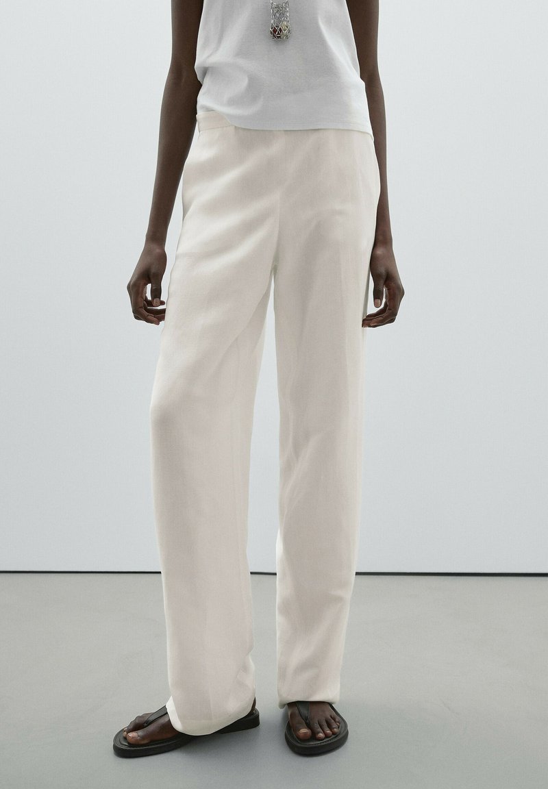 Wide-leg trousers in soft white fabric, featuring a smooth texture and simple design. Paired with black flip-flops and a light top.