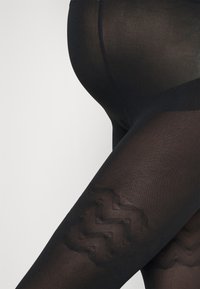 Neprozorni črni leggingi z teksturiranim zigzag vzorcem na spodnjem delu noge, ki se odlikujejo z gladko površino in elegantnim dizajnom.