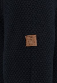 Tessuto nero con texture a nido d'ape, con un'etichetta in pelle marrone cucita su un lato.