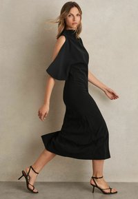 Schwarzes Midikleid mit kalten Schultern, hohem Ausschnitt, ausgestellt kurzen Ärmeln und glatter Textur. Kombiniert mit schwarzen Riemchenschuhen.