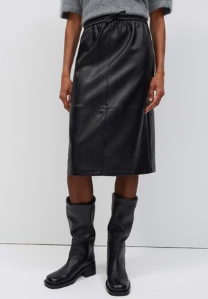Zwarte nepleren rok tot op de knie met een elastische tailleband en zwarte losse halfhoge laarzen bij een persoon.
