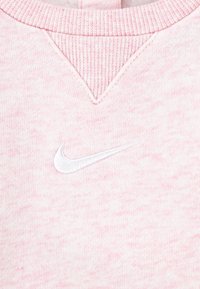 Svetloružový sveter vyrobený z mäkkej látky, s V-výstrihom a bielym vyšitým logom Nike na prednej strane.