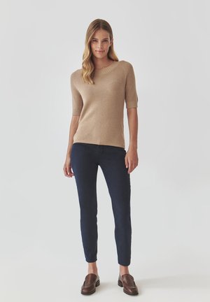 Beige ribbed sweater with short sleeves, paired with navy slim-fit jeans and brown slip-on shoes, featuring a simple, clean design.