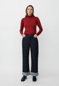 Rode longsleeve coltrui gecombineerd met donkerblauwe wijde jeans met grote manchetten die lichter van kleur zijn. Zwarte schoenen.