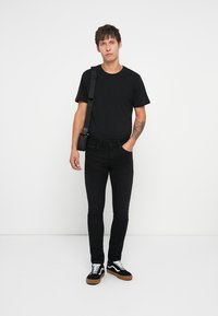 Crna majica, crne slim-fit traperice i crne tenisice s bijelim detaljima. Osoba nosi malu crnu torbicu preko tijela.