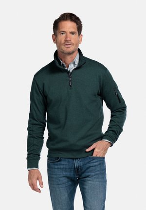 Donkergroen pull met rits en lange mouwen, gemaakt van gemêleerd stof. Heeft een zijrits zak en een gelaagde kraag over een patroon shirt.