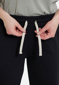 Svarta joggingsbyxor med elastisk midja och beige snöre. Materialet verkar mjukt med en slät yta och sidfickor.