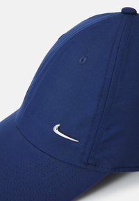 Sötétkék Nike sapka, textilből készült, ezüst színű swoosh logóval, strukturált csúccsal és látható varrási részletekkel a koronán és a karimán.