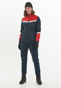 Marineblauwe en rode sportjacket met witte strepen, ritssluiting, gecombineerd met marineblauwe broek, zwarte handschoenen en laarzen. Kenmerkt zich door een modern en functioneel ontwerp.