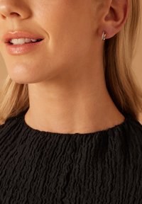 Zilveren ringoorbellen met een gestructureerd oppervlak, voorzien van glinsterende accenten, gedragen door een persoon met halflang blond haar.