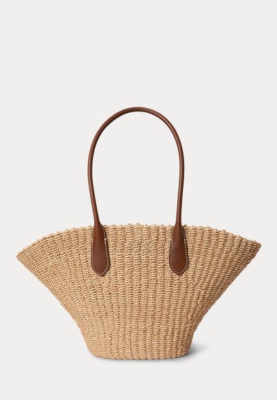 Fonott szalma táska széles felső résszel és két hosszú barna bőrfogantyúval, egyszínű háttéren.