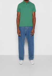 Green polo shirt with short sleeves, paired with light blue loose-fitting jeans and white sneakers. Icon logo on the left chest.