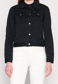 Black denim jacket with a snap-button front, two chest pockets, a pointed collar, and a cropped design. Soft texture with subtle stitching details.