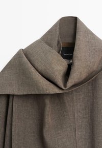 Manteau en tissu marron texturé avec un large col replié et une fermeture éclair visible sous le col, étiqueté Massimo Dutti.