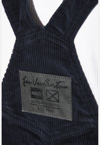 Marinefarbene Corduroy-Latzhosen aus strukturiertem Stoff mit einem schwarzen Lederetikett, das den Markennamen und Symbole zeigt, sowie gesteppten Details.