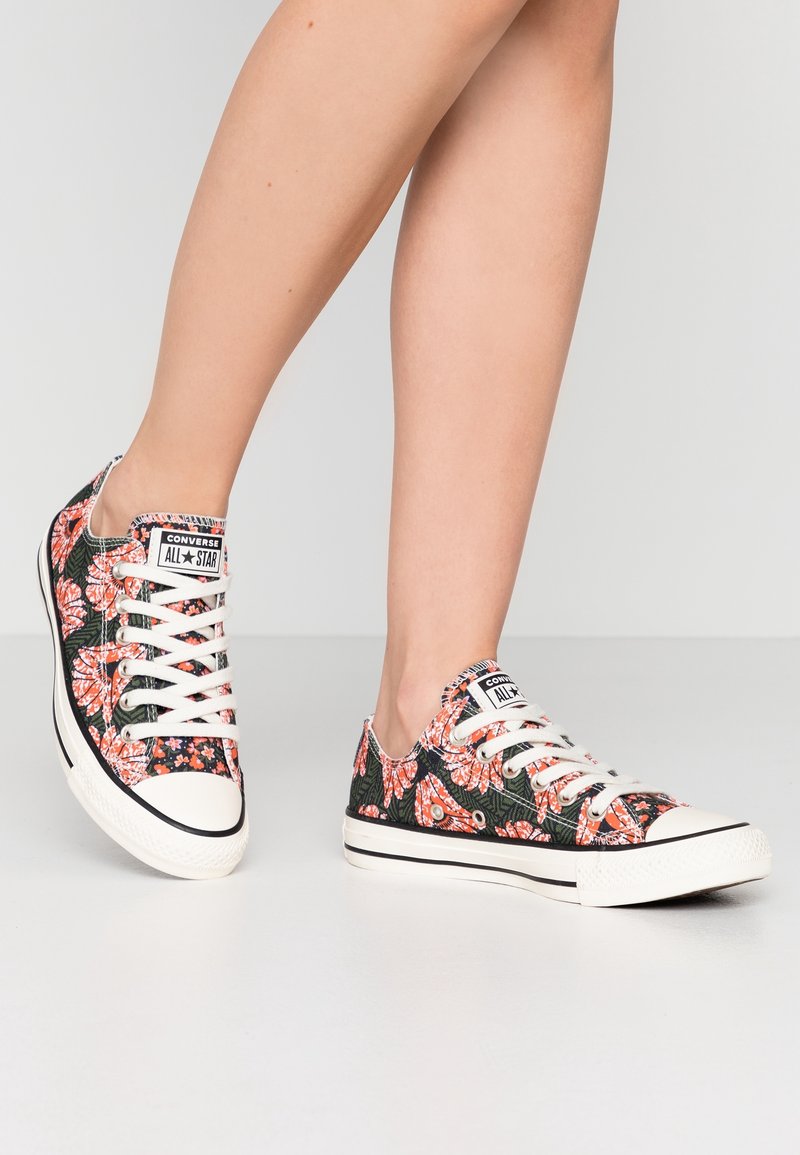 Baskets Converse All Star avec un motif floral noir comportant des fleurs orange, des lacets blancs, un capuchon en caoutchouc et un tissu texturé.