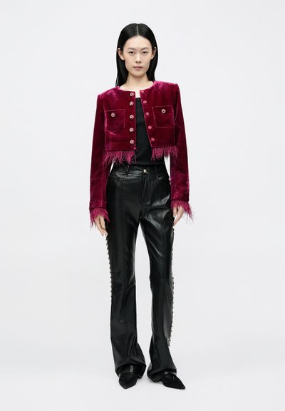 Lühendatud burgundia punane sametjakk tutikujulise äärise, esitaskute ja dekoratiivsete nööpidega, sobitatud mustade nahast laiade pükstega.