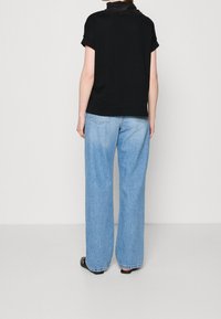 Top negro de manga corta con un cuello alto, combinado con jeans de pierna ancha en azul claro. Tejido suave con un corte relajado. Zapatos negros.