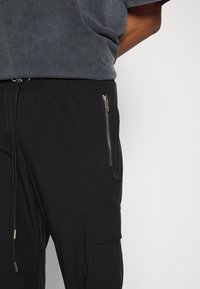 Svarta cargobyxor med dragsko i midjan, ficka med dragkedja, slät textur och konisk benform. Passar för vardagsbruk.