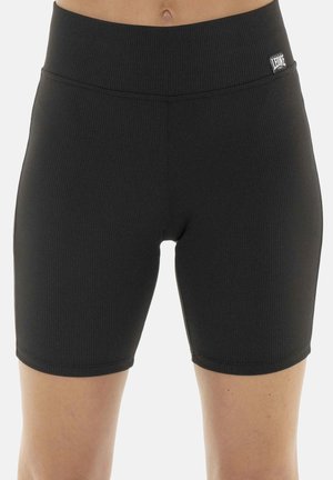 Partie médiane portant un short de cycliste noir côtelé taille haute avec un petit patch logo blanc sur le côté droit de la ceinture.
