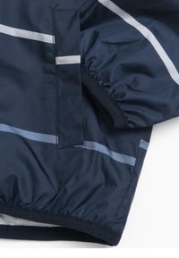 Veste bleu marine avec des rayures horizontales gris clair. Présente des poignets élastiques, une poche zippée et un tissu lisse, résistant à l'eau.