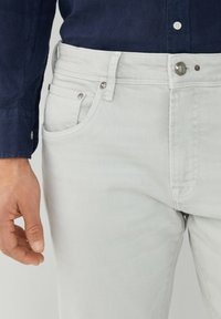 Jeans de mezclilla en un gris claro con un corte clásico, diseño de cinco bolsillos, cierre frontal de botón y detalles en tono plateado.