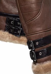 Braune Lederjacke mit schwarzen Akzenten, Schnallen und Schafslederfutter. Texturierte Oberfläche mit gesteppten Details und metallischen Beschlägen.