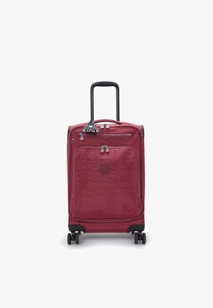 Červený kufr s texturovaným povrchem, dvěma zipy a sklopnou černou rukojetí. Má čtyři kolečka a dekorativní klíčenku.