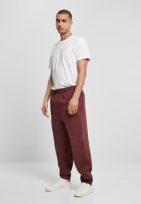 Tricou alb cu mânecă scurtă și buzunar frontal, asortat cu pantaloni jogger bordeaux cu talie elastică și mansete, și teniși albi.