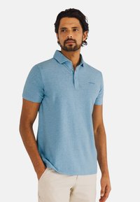 Lichtblauw polo t-shirt met korte mouwen en een kraagdesign, gemaakt van een gestructureerde stof. Subtiele logo op de borst, gecombineerd met lichte broek.