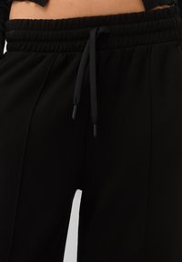 Svarta sweatpants har ett elastiskt midjeband med dragsko, mjuk textur och sidofickor för komfort och rörlighet.