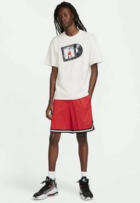 Fehér pamut póló grafikával és rövid ujjakkal, piros szintetikus rövidnadrággal, fekete szegéllyel és logóval párosítva.