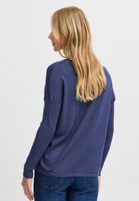 Pulover din lână de culoare albastru marin, cu mâneci lungi și croială lejeră, manșete ribbate și textură moale. Are un guler rotund și detalii pe cusătura din spate.