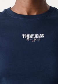 Tamsiai mėlynas medvilninis marškinėlis su apvalia iškirpte, turintis baltą tekstinį logotipą „TOMMY JEANS New York“ krūtinėje. Lygus paviršius, neformalus dizainas.