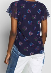 Navy blue short-sleeve blouse featuring colorful floral patterns. Sheer fabric at sleeves with rounded hem and relaxed fit.