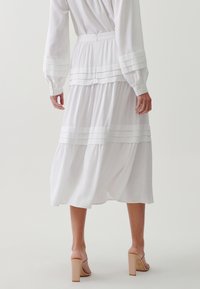 Falda midi blanca de capas con rayas horizontales, hecha de una tela ligera. Incluye una cinturilla ajustada y se combina con sandalias de tacón cuadrado.