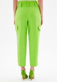 Groene cargobroek met een getailleerde pasvorm, voorzien van zijzakken, een riem en een cropped leg ontwerp. Gecombineerd met groene hoge hakken.