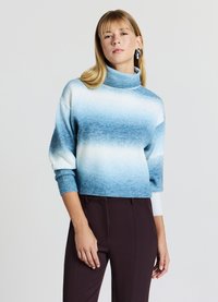 Maglione accorciato in tonalità blu sfumate, con colletto alto, polsini a costine e texture morbida. Abbinato a pantaloni scuri e su misura.