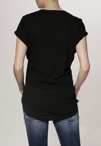 Svart t-shirt med kort ärm och rund halsringning, i avslappnad passform, med omslagda ärmslut och en längre bakre fåll. Mjuk tygkvalitet.