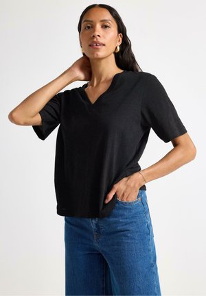 Black, short-sleeve V-neck top in lightweight fabric. Relaxed fit with a slight drape, paired with high-waisted blue jeans.