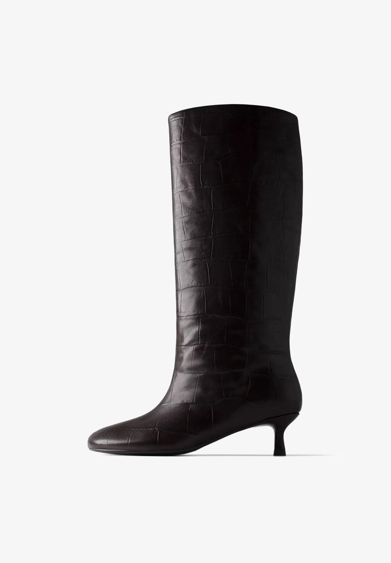 Botte noire femme montante jusqu’au genou avec petit talon kitten et motif crocodile embossé, présentée sur fond blanc.