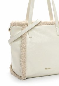 Krémsvětlá taška přes rameno z umělé kůže s lemováním ze sherpy, dvěma držadly, popruhem přes rameno a malým zlatým logem značky na přední straně.