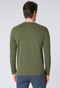 Camicia a maniche lunghe color verde oliva realizzata in tessuto morbido, con scollatura rotonda e un design semplice senza decorazioni.