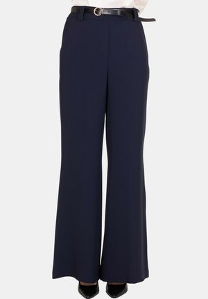 Pantaloni ampi navy con cintura nera, abbinati a scarpe nere con punta appuntita e camicetta bianca infilata dentro.