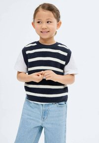 Top senza maniche a righe navy e bianche, indossato su una t-shirt bianca, abbinato a jeans in denim azzurro chiaro. Design semplice e casual.