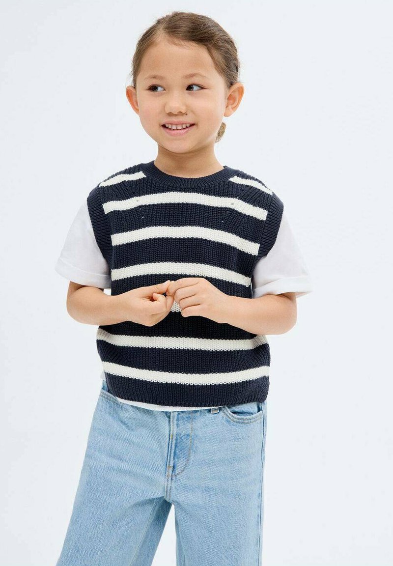 Top senza maniche a righe navy e bianche, indossato su una t-shirt bianca, abbinato a jeans in denim azzurro chiaro. Design semplice e casual.