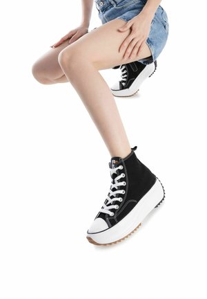 Zapatillas altas negras con cordones blancos, puntera blanca y suela gruesa blanca. Parte superior de lona texturizada con suela de goma y costuras de acento.