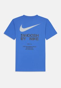Sinine puuvillane T-särk, millel on suur hõbedane Nike swoosh logo ja must tekst "SWOOSH BY NIKE" seljal. Lühikesed varrukad ja ümmargune kaelus.
